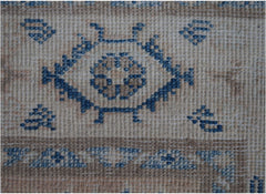A close-up of an Afghan Kazakh runner rug featuring a blue geometric floral motif on a beige base.