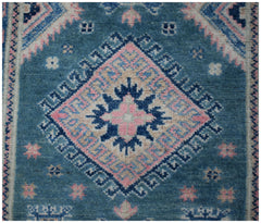 A handmade Afghan Kazakh runner featuring a central diamond medallion in blue, pink, and cream.