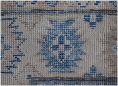 A close-up of a handmade Afghan Kazakh runner featuring blue geometric motifs on a beige wool field.