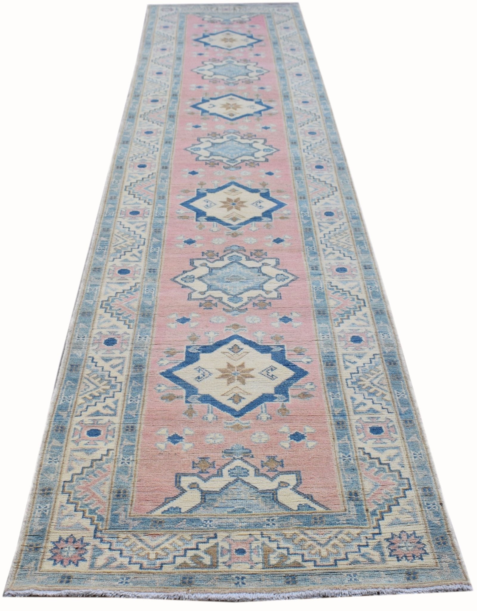 A handmade Afghan Kazakh runner rug featuring a pink field with repeating blue geometric medallions.