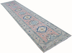 A handmade Afghan Kazakh runner rug featuring geometric patterns in soft pink and blue tones.