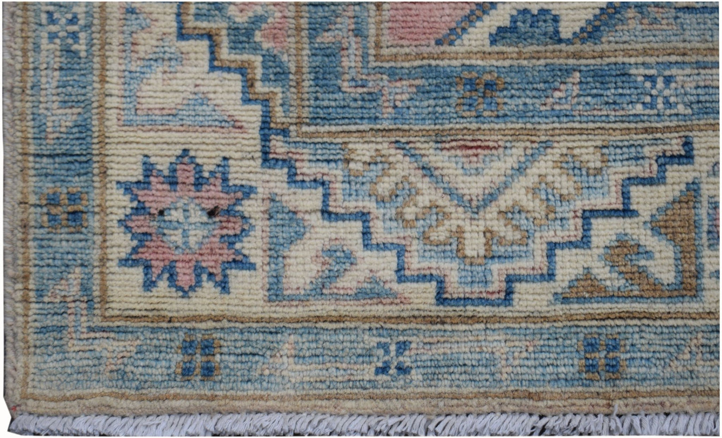 A handmade Afghan Kazakh runner featuring geometric patterns in blue, pink, and cream wool.