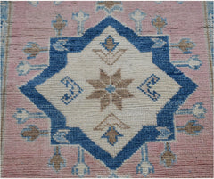 A handmade Afghan Kazakh runner featuring a central blue star motif on a pink wool background.
