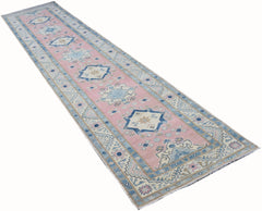A handmade Afghan Kazakh runner rug featuring a pink field with blue and beige geometric motifs.