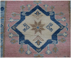 An Afghan Kazakh runner rug featuring a central blue and beige star medallion on a pink field.