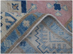 A close-up of a handmade Afghan Kazakh runner featuring a geometric pattern in blue, pink, and beige.
