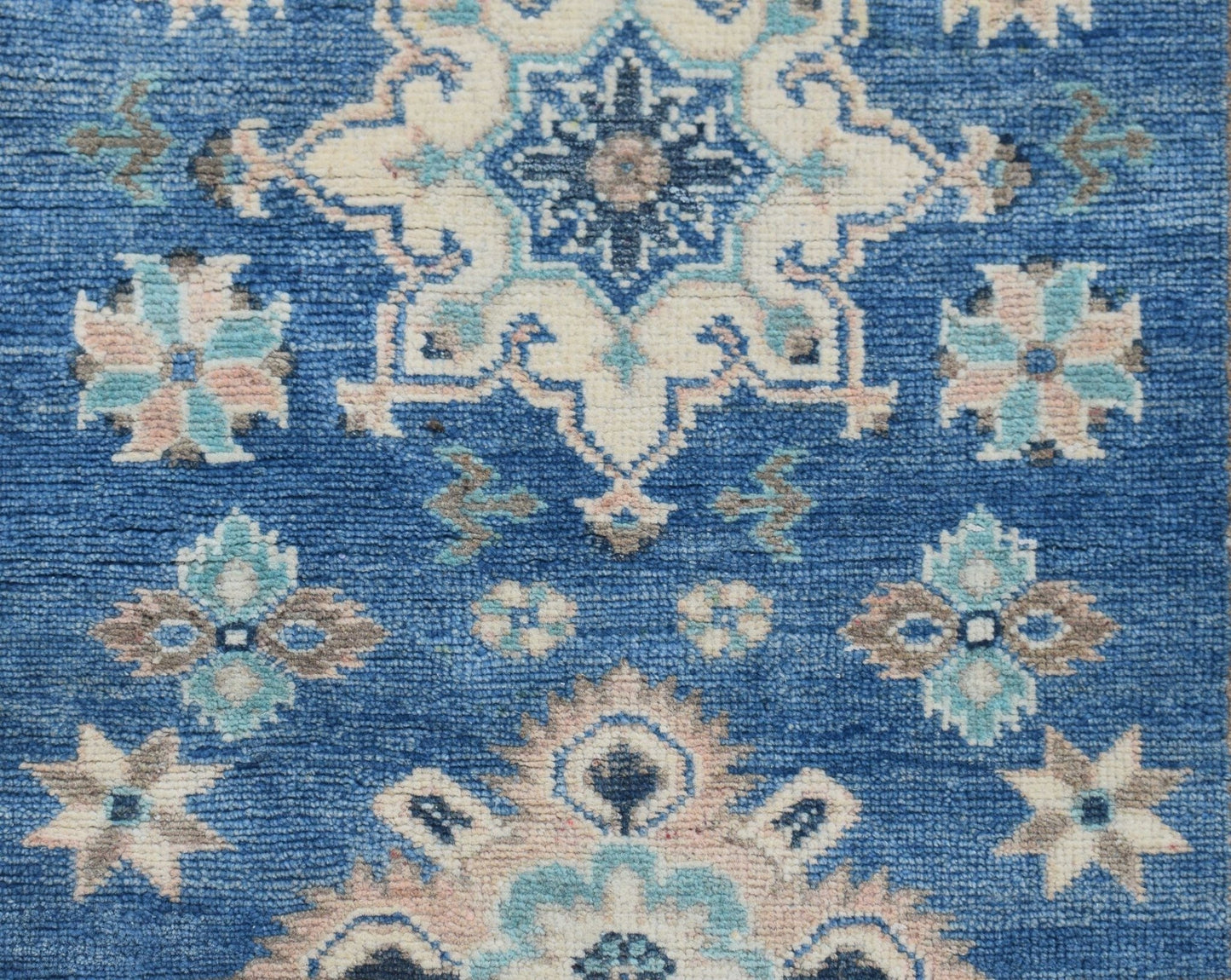 A handmade Afghan Kazakh runner rug featuring a blue field with intricate beige and grey motifs.