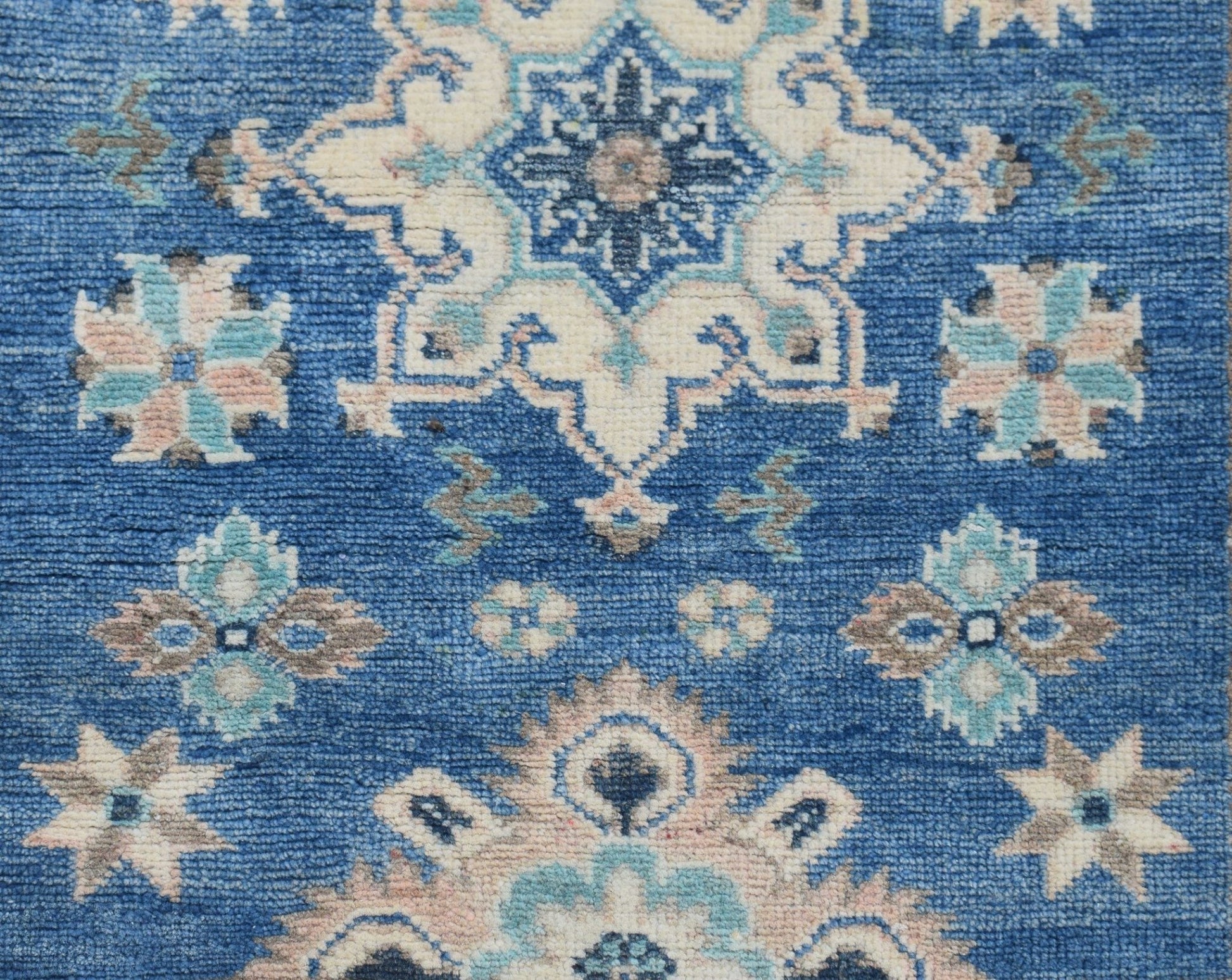 A handmade Afghan Kazakh runner rug featuring a blue field with intricate beige and grey motifs.