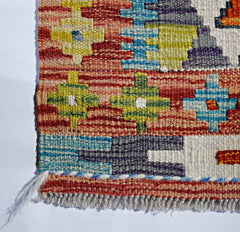 A handwoven Afghan Maimana kilim featuring a geometric pattern in vibrant multicolored wool.