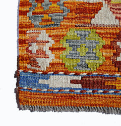 A close-up of a handmade Afghan Maimana kilim featuring geometric patterns in orange and green.