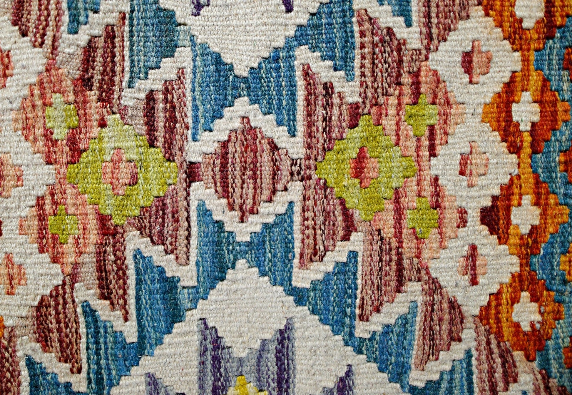 A close-up of a handmade Afghan Maimana kilim featuring a vibrant geometric pattern in wool.