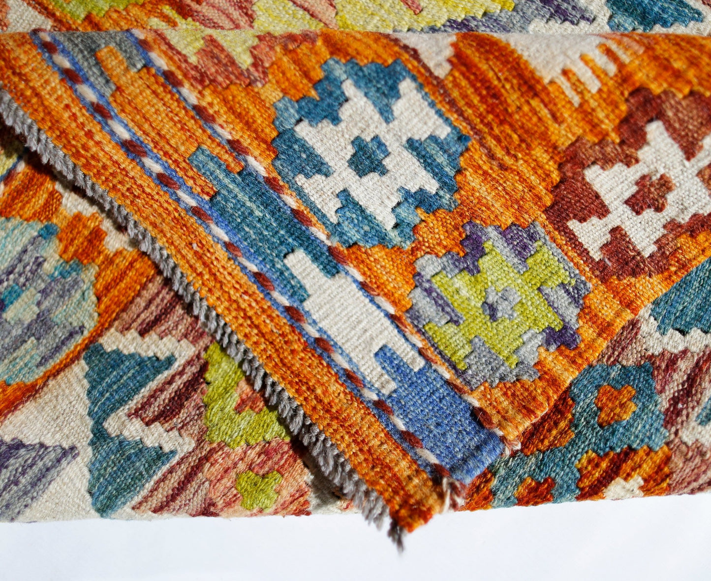 A folded Afghan Maimana kilim featuring vibrant geometric patterns in wool.