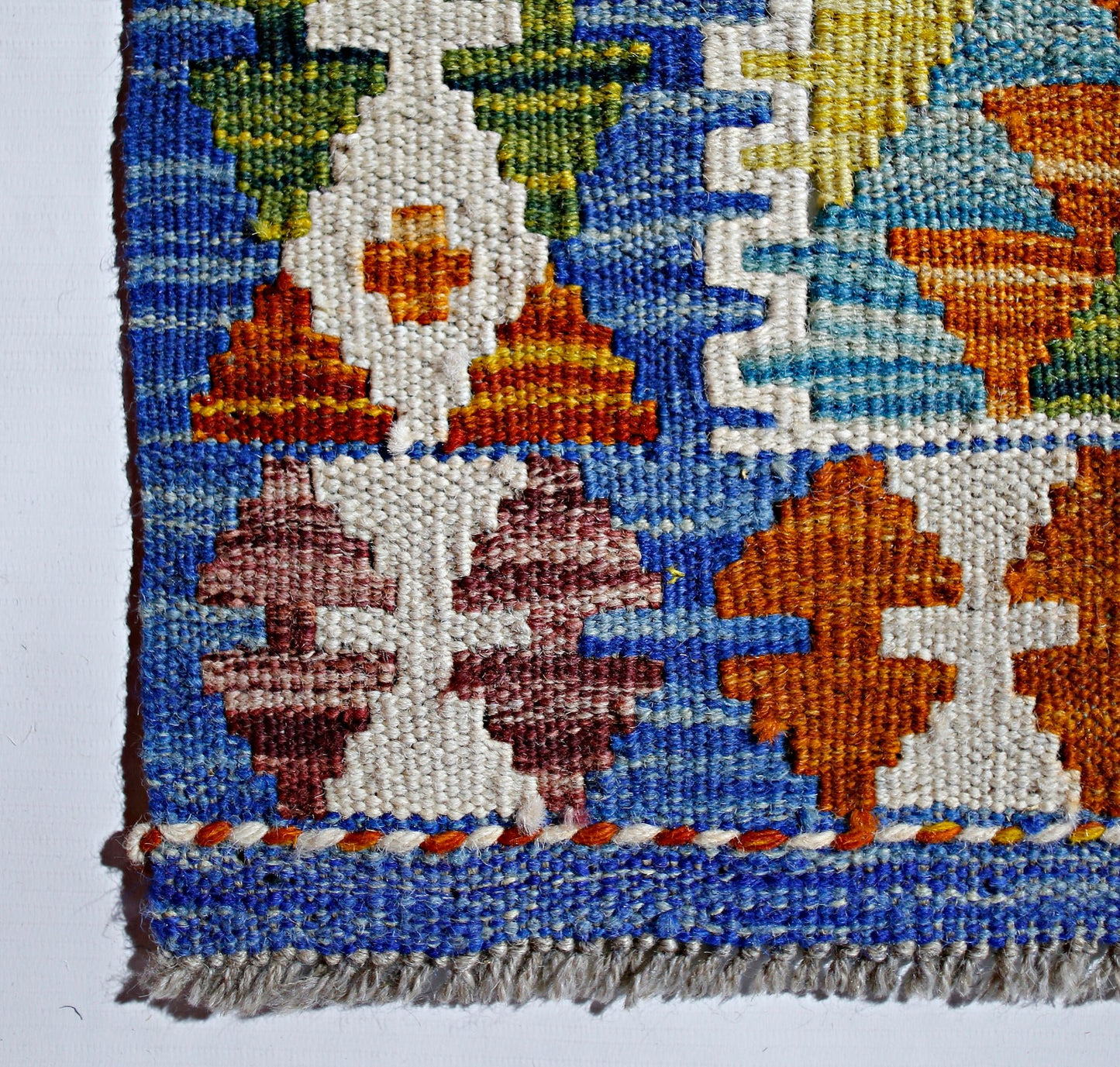 A close-up of a handmade Afghan Maimana kilim featuring geometric patterns in blue, white, and orange.