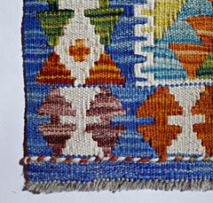 A close-up of a handmade Afghan Maimana kilim featuring geometric patterns in blue, white, and orange.