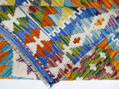 A folded Afghan Maimana kilim rug featuring a vibrant, handwoven geometric pattern in wool.