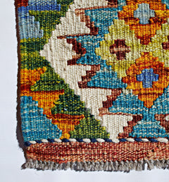 A close-up of a handmade Afghan Maimana kilim featuring vibrant geometric patterns in wool.