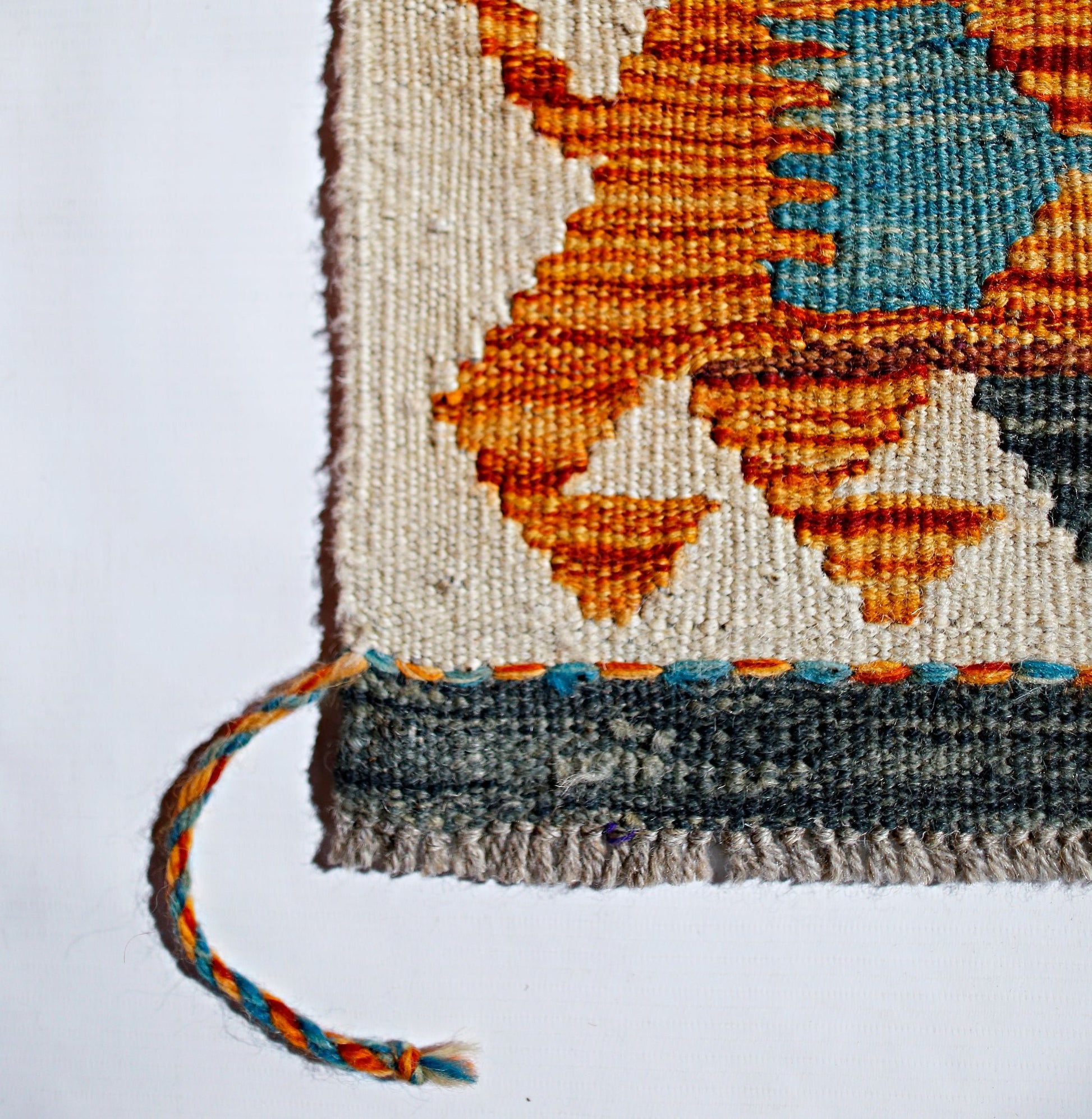 A close-up of a handwoven Afghan Maimana kilim featuring geometric orange and blue wool patterns.
