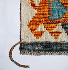 A close-up of a handwoven Afghan Maimana kilim featuring geometric orange and blue wool patterns.