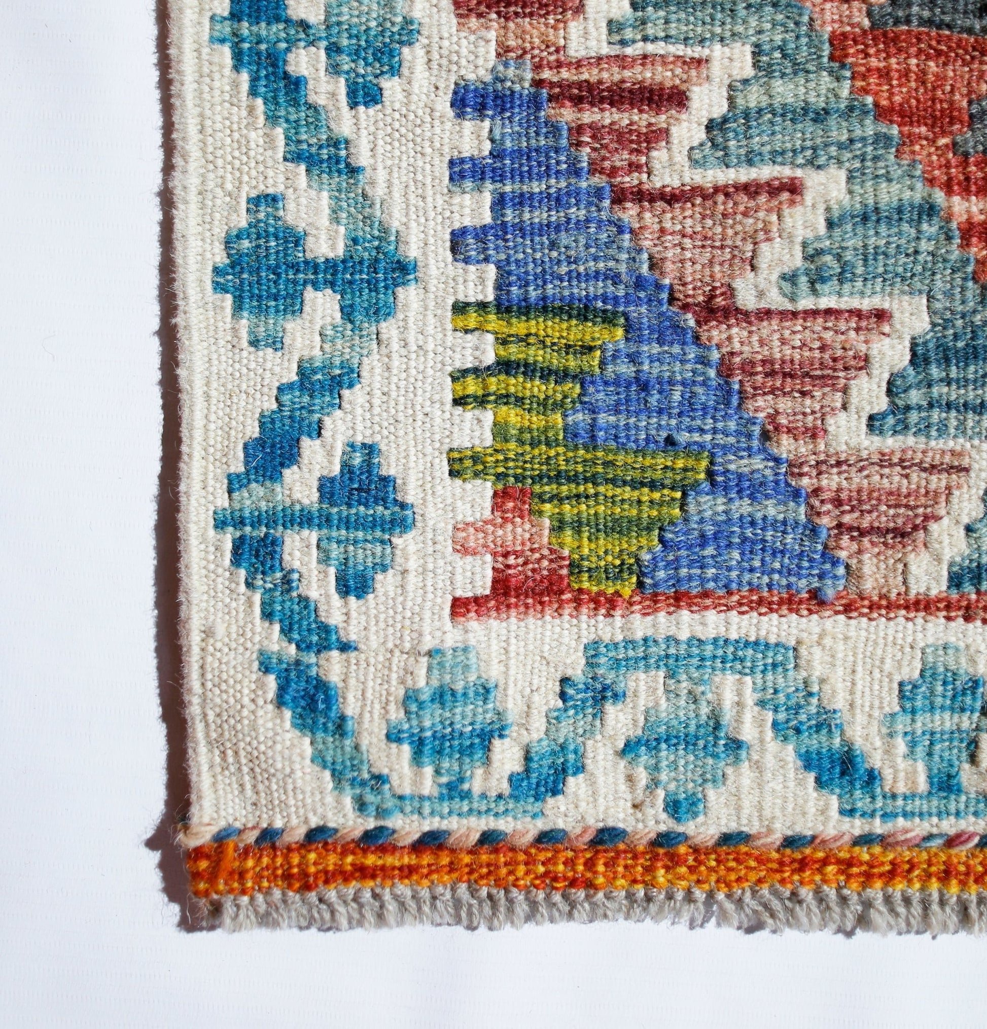 A close-up of a handmade Afghan Maimana kilim featuring geometric patterns in blue, red, and green.