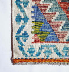 A close-up of a handmade Afghan Maimana kilim featuring geometric patterns in blue, red, and green.