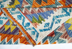 A folded Afghan Maimana kilim rug featuring vibrant geometric patterns in wool.