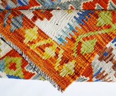 A folded Afghan Maimana kilim rug featuring a vibrant geometric pattern in wool.
