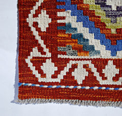 Handwoven Afghan Maimana kilim featuring geometric patterns in vibrant red, blue, and white wool.