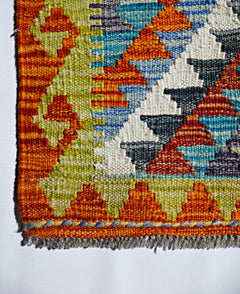 A handmade Afghan Maimana kilim featuring a vibrant geometric pattern in wool.
