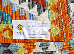 A handwoven Afghan Maimana kilim featuring a vibrant geometric pattern in orange, blue, and cream.