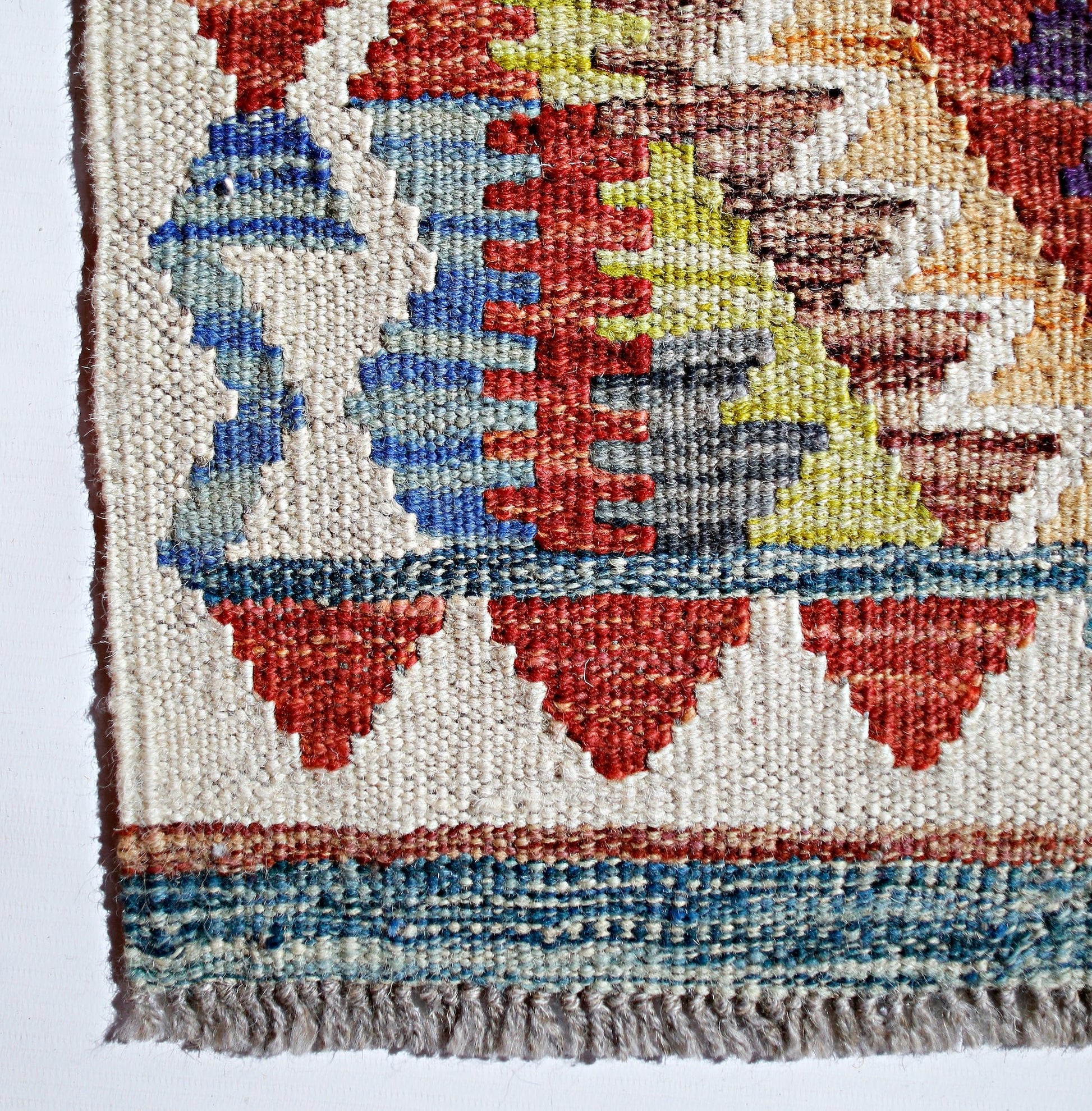 A close-up of a handmade Afghan Maimana kilim featuring geometric patterns in red, blue, and yellow.