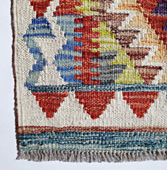 A close-up of a handmade Afghan Maimana kilim featuring geometric patterns in red, blue, and yellow.