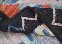 A folded Afghan Maimana kilim rug featuring a geometric pattern in black, blue, and orange wool.