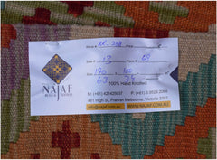 An Afghan Maimana Kilim rug featuring a geometric pattern in vibrant orange, green, and purple tones.