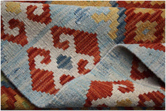 A handmade Afghan Maimana kilim rug featuring a geometric pattern in red, blue, and yellow wool.