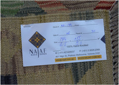 A close-up view of the back of an Afghan Maimana Kilim rug with a product information tag attached.