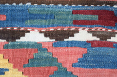 A close-up of a handmade Afghan Maimana kilim featuring geometric patterns in blue, red, and yellow.