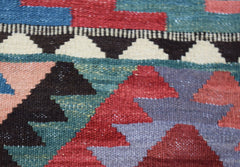 A close-up of a handmade Afghan Maimana kilim featuring geometric patterns in red, blue, and green.