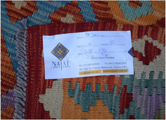 An Afghan Maimana Kilim rug featuring a geometric pattern in vibrant orange, blue, and purple.