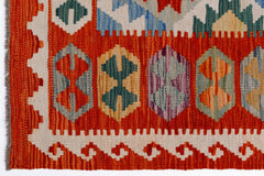 A handwoven Afghan Maimana kilim featuring geometric motifs in vibrant orange, blue, and green.