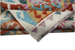 A handwoven Afghan Maimana kilim rug featuring a colorful geometric pattern and fringed edges.
