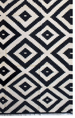 A handmade Afghan Maimana kilim rug featuring a repeating black and cream geometric diamond pattern.