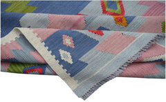 A handwoven Afghan Maimana kilim rug featuring geometric patterns in blue, pink, and green wool.