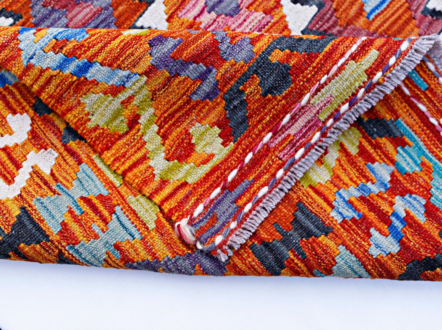 A folded Afghan Maimana kilim featuring a vibrant geometric pattern in wool.