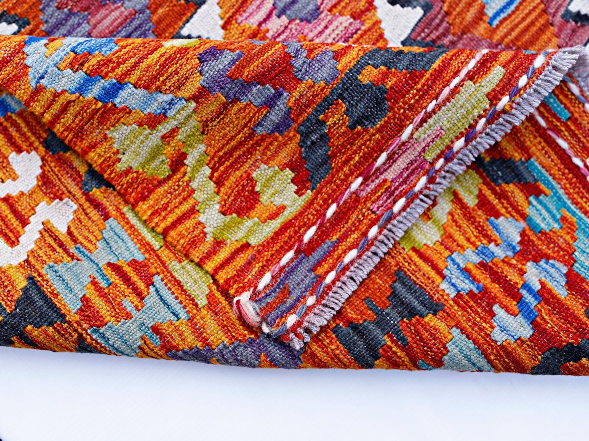 A folded Afghan Maimana kilim featuring a vibrant geometric pattern in wool.
