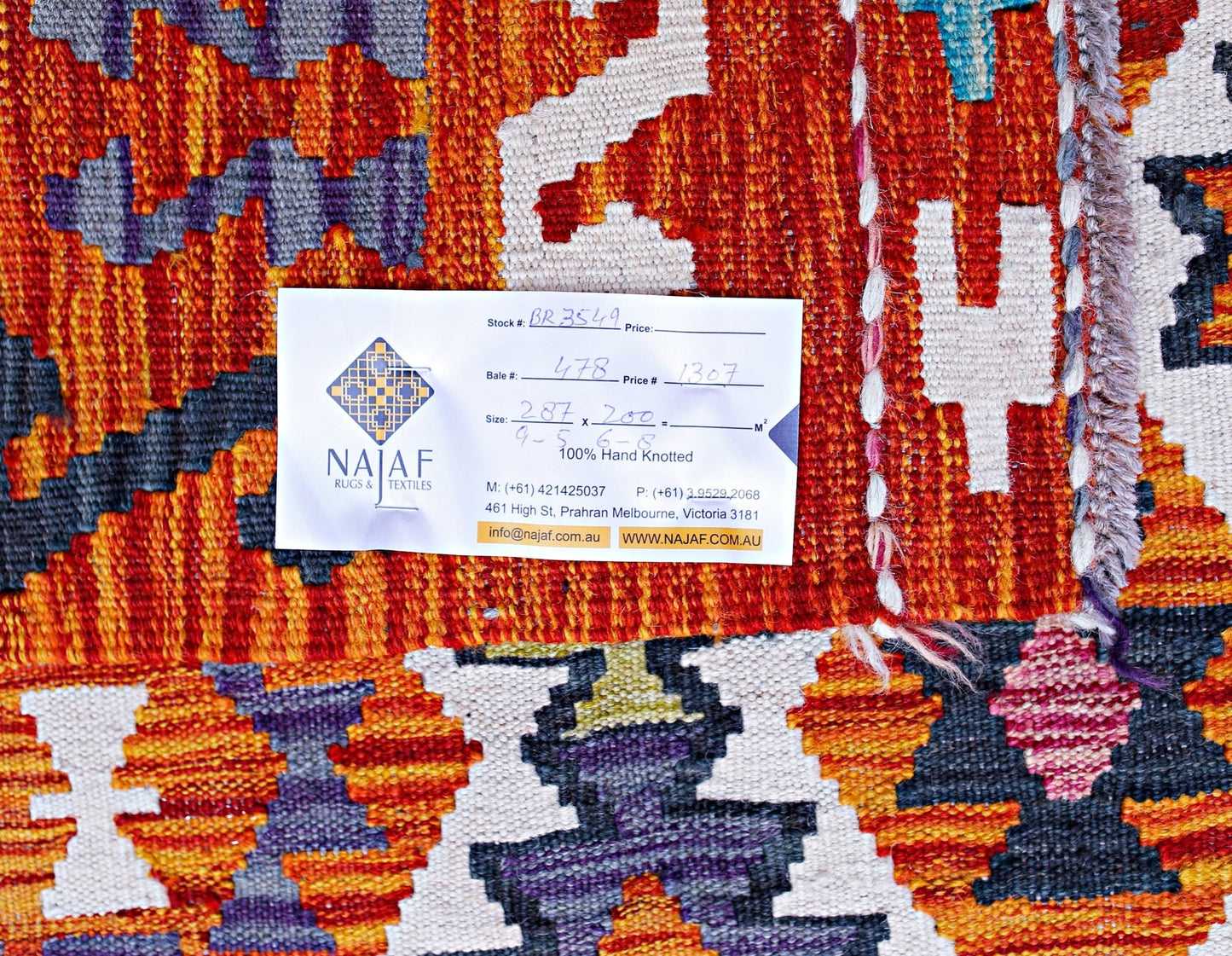 A handwoven Afghan Maimana kilim featuring a vibrant geometric pattern in orange, blue, and white.