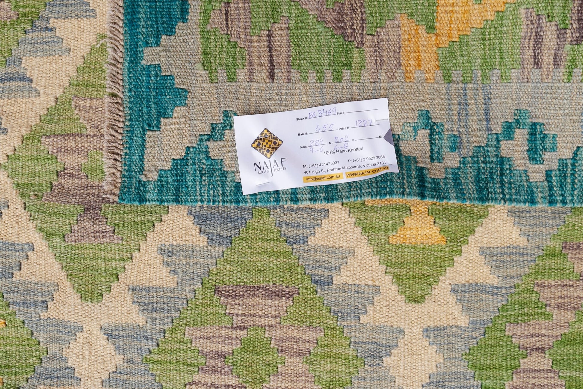 An Afghan Maimana kilim rug featuring a geometric pattern in shades of green, blue, and yellow.
