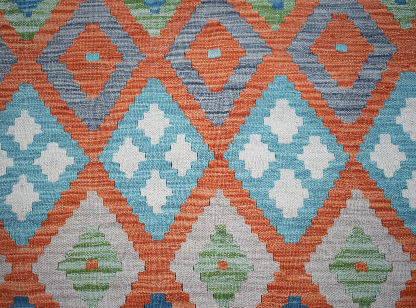 Handwoven Afghan Maimana kilim featuring a vibrant geometric pattern in orange, blue, and green.