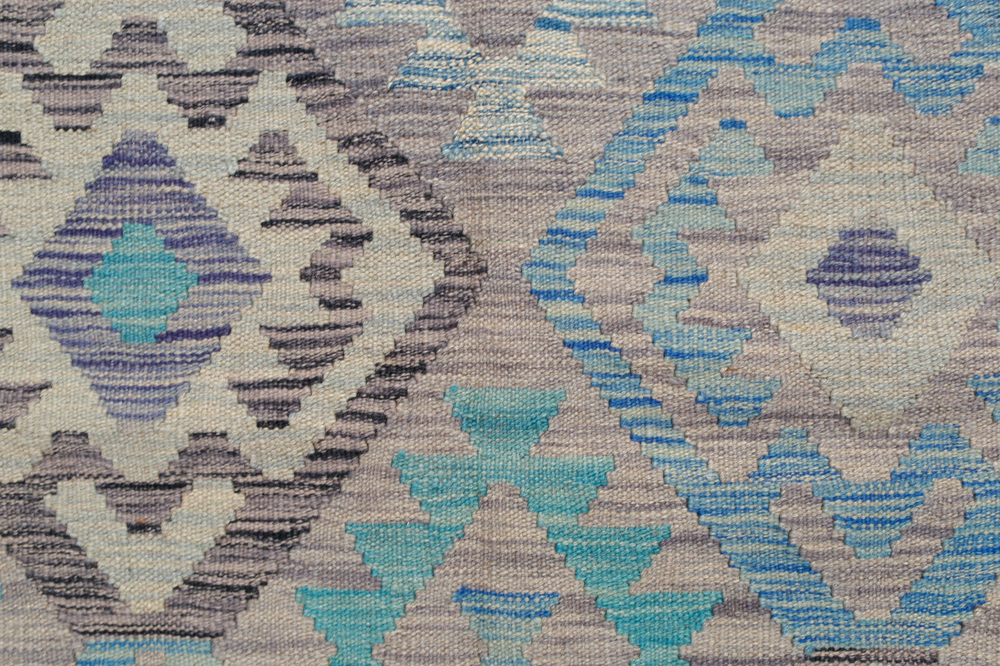 A handwoven Afghan Maimana kilim rug featuring a geometric pattern in shades of blue and grey.