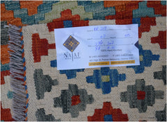 An Afghan Maimana Kilim rug featuring a geometric pattern in red, blue, and green on a cream base.