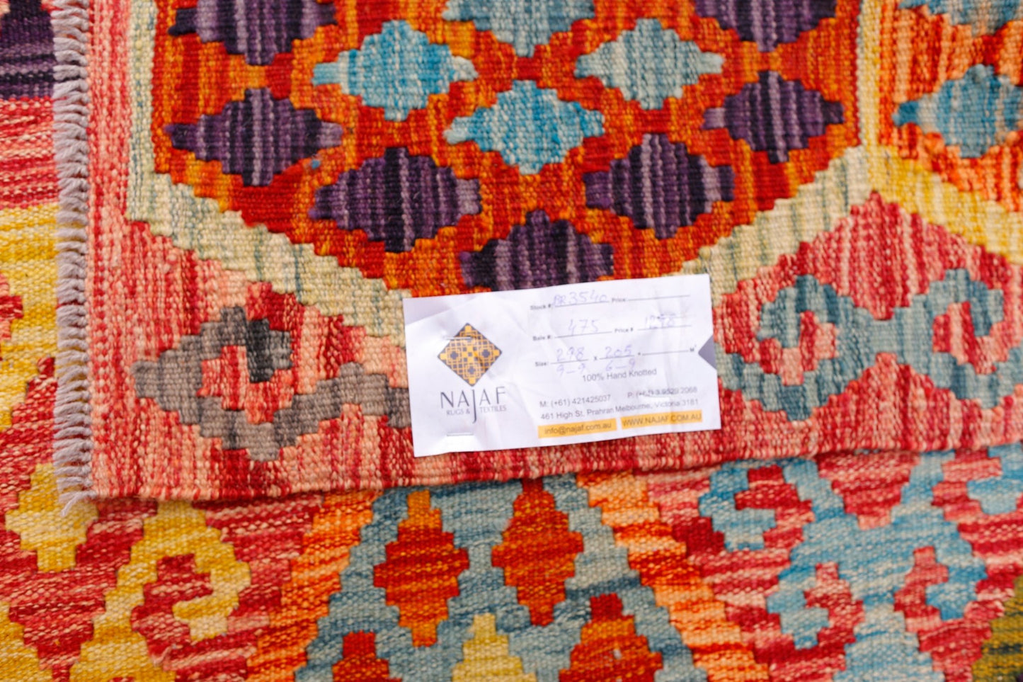 A handwoven Afghan Maimana kilim featuring a vibrant geometric pattern in red, blue, and purple.